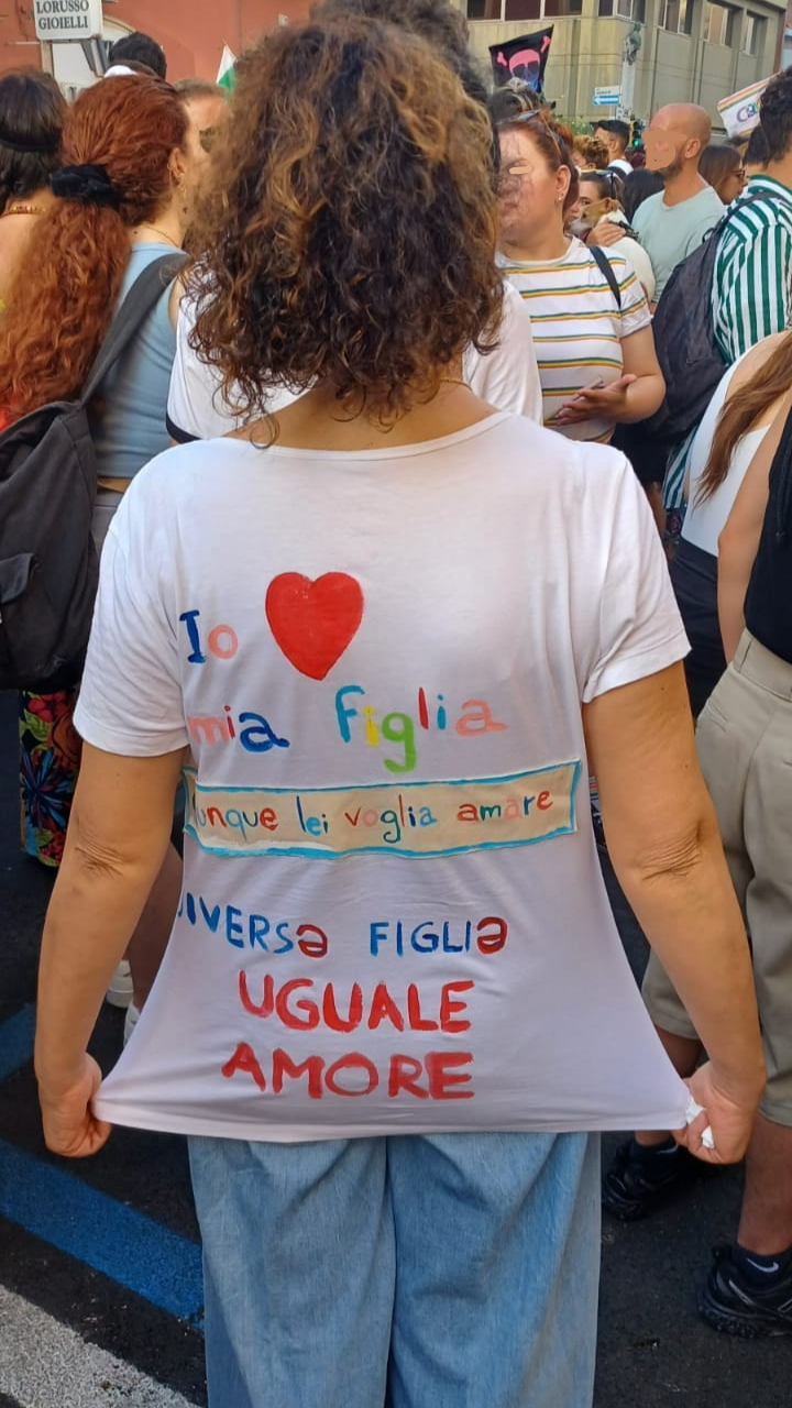 Persona di spalle mostra il retro di una maglietta con scritta "Io amo mia figlia chiunque lei voglia amare, divers figl uguale amore"